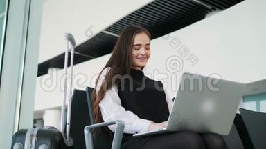 机场年轻女乘客在候机大厅坐着智能手机和笔记本电脑，等待她的航班、工作